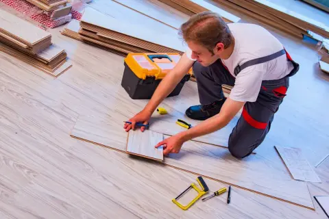 Fachowiec układa panele podłogowe, zastanawiając się, ile za położenie paneli. Narzędzia i materiały czekają na użycie.