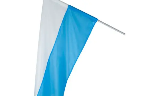 Biało-niebieskie flagi kościelne na maszcie, gotowe do procesji lub uroczystości.