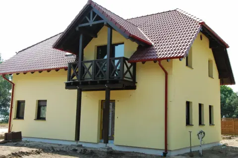 Jasnożółty dom z czerwonym dachem i drewnianym balkonem.
