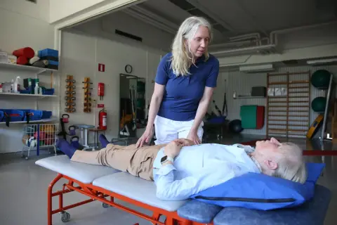 Fysioterapeut undersöker en patient som ligger på en brits. Patienten verkar vara fixerad bebis i sin position, redo för behandling.