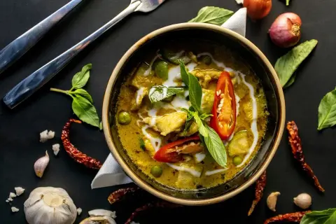 Aromatyczne curry z kurkumą, pełne zielonych warzyw i kawałków kurczaka, ozdobione chili i bazylią.