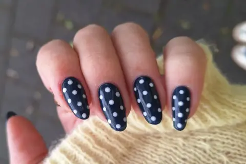 Manucure élégante avec un nail art pois sur fond bleu marine. Les ongles sont ornés de petits ronds blancs, créant un look ludique et chic.