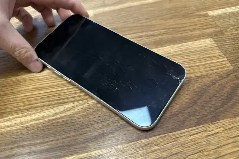 Dłoń trzyma telefon z pękniętym szkłem hartowanym. Ekran pokryty jest siecią drobnych pęknięć, szczególnie widocznych w prawym dolnym rogu.