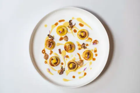 Piccolo capolavoro culinario: tartellette dorate con ripieno giallo, guarnite con calamari croccanti e fiori viola. Un'opera d'arte degna di un ristorante con massimo stelle Michelin.
