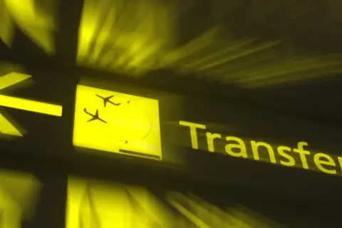 Żółty znak lotniskowy z ikoną samolotu i napisem "Transfer". Czy można opuścić lotnisko podczas przesiadki?