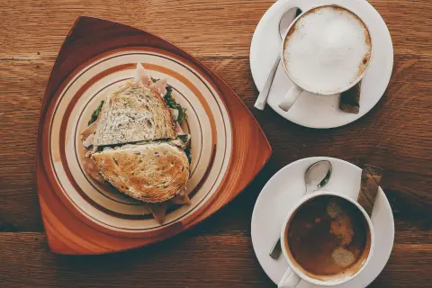 Ein Sandwich und zwei Kaffees auf einem Holztisch. Der Kaffee könnte mit Kaffeesirup verfeinert werden.