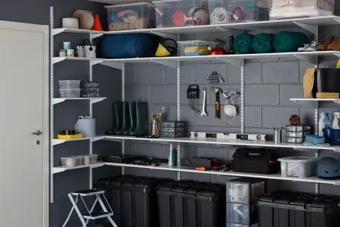 Estanterías metálicas con todo tipo de objetos: cajas, herramientas, botas de agua, botellas. Un ejemplo de cómo organizar un trastero.