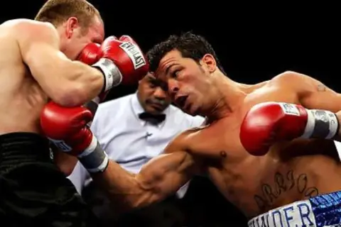 Boxer lands a powerful body shot, his opponent recoils as the referee watches closely.