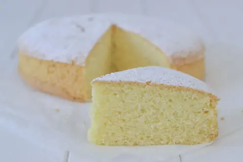 Una soffice torta con farina di riso, spolverata di zucchero a velo, con una fetta tagliata.