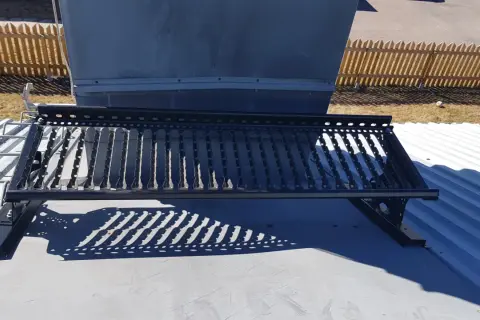 En takbrygga framför en stor ventilationsanläggning, liknande en skorsten. Solen kastar ett mönstrat skuggspel.