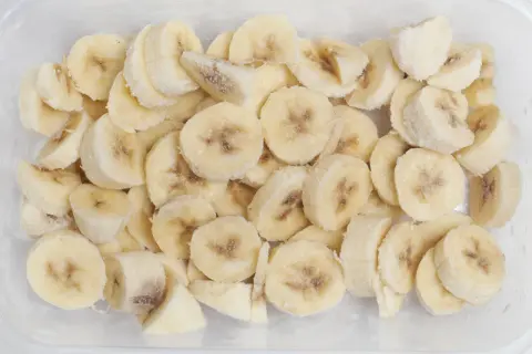 Pokrojone w plasterki banany w pojemniku, gotowe do mrożenia. To dowód, że banany można mrozić, idealne do smoothie!