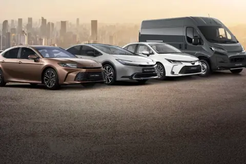 Różnorodne modele Toyota: brązowa Camry Hybrid, srebrny Prius Plug-in Hybrid, biała Corolla i szary Proace Max na tle miasta.