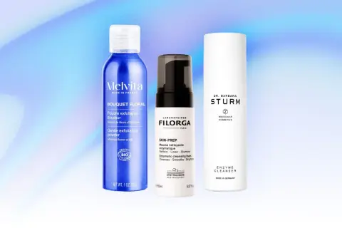 Tre flaconi di prodotti per la cura della pelle, tra cui una polvere esfoliante e due detergenti enzimatici, su sfondo blu sfumato.