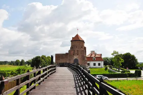Drewniany most prowadzi do ceglanego zamku z czerwoną wieżą. Idealne ciekawe miejsca 100km od Warszawy na weekendową wycieczkę.