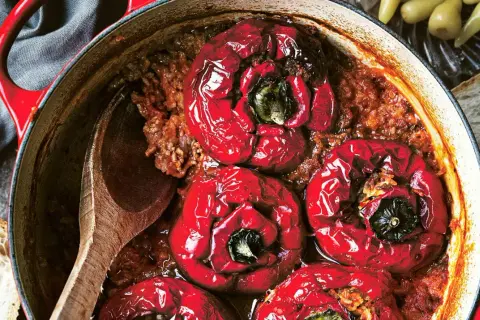 Röda, fyllda paprikor i en gryta med köttfärs och ris, redo att serveras med en träsked och en bit bröd.