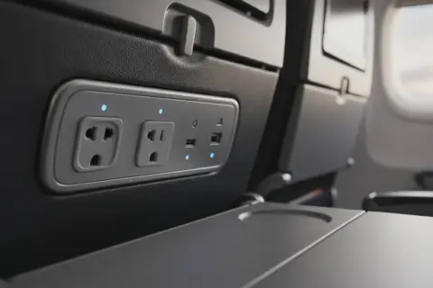W samolotach są gniazdka! Widok na panel z gniazdkami elektrycznymi i portami USB w fotelu samolotowym, gotowy do ładowania urządzeń.