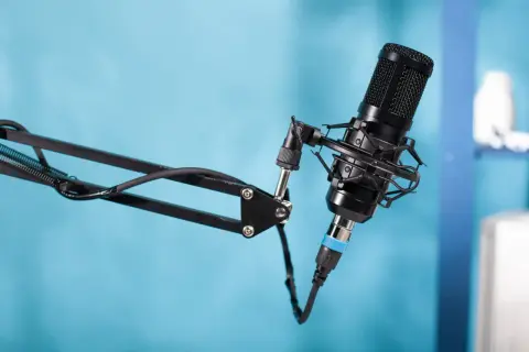 Czarny mikrofon pojemnościowy na wysięgniku, gotowy do nagrania podcastu. W tle niebieskie tło.