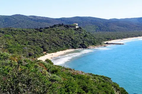Spiaggia delle bandite di Scarlino, con mare azzurro, pineta lussureggiante e una villa in collina.