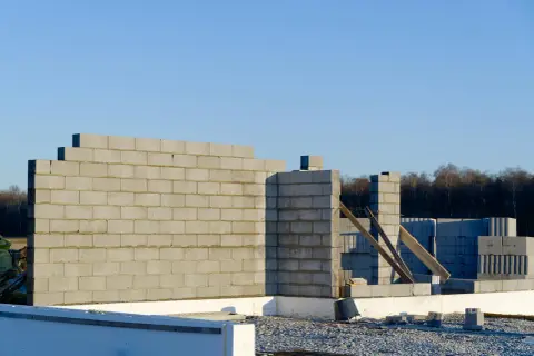 Budowa domu w toku. Wznoszona jest ściana nośna z bloczków betonowych, widoczne fundamenty i materiały budowlane.