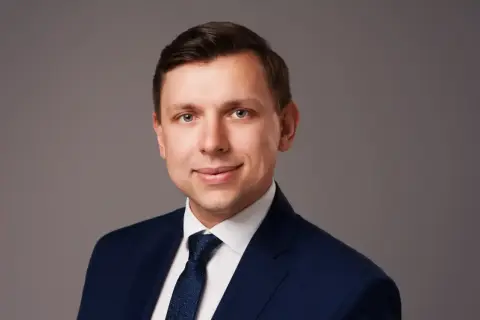 Portret mężczyzny w granatowym garniturze i krawacie na szarym tle.