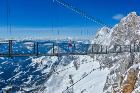 Most na Dachstein Glacier, gdzie turystka podziwia zimowy krajobraz Alp.