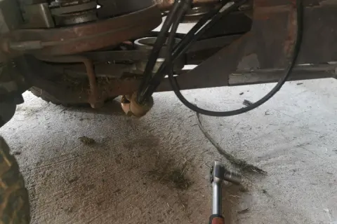 Jak założyć pasek do kosiarki traktorka Husqvarna? Widok mechanizmu napędowego z kluczem nasadowym.
