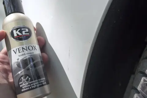 Jak usunąć rysy z samochodu domowym sposobem? Butelka K2 VENOX Scratch remover obok zarysowanego lakieru.
