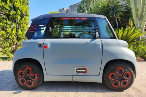 Citroën Ami grigia parcheggiata all'aperto, con dettagli rossi e neri. La scritta "Autoscuola Contarino" sul finestrino suggerisce un uso per l'apprendimento, con un'ottima **citroen ami autonomia** per la città.
