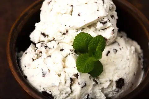Cremiges Stracciatella Eis mit Schokoladenstückchen in einer Holzschale, garniert mit frischer Minze. Ein einfaches Stracciatella Eis Rezept zum Nachmachen.