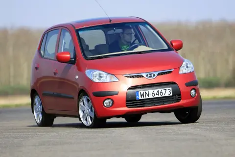 Czerwony Hyundai i10 na drodze. Kierowca w okularach i zielonym szaliku. Wiele pozytywnych hyundai i10 opinie potwierdza jego miejski charakter.