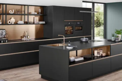 Cocina moderna con isla central, gabinetes negros, detalles dorados y electrodomésticos integrados.