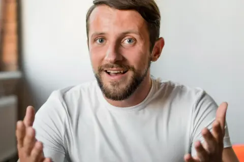Mężczyzna z brodą i niebieskimi oczami, gestykulując, jakby zastanawiał się, czy mówienie do siebie jest normalne.