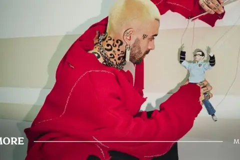 Quebonafide w czerwonym swetrze steruje marionetką, jakby tworzył swoje utwory.