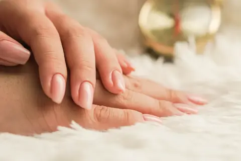 Mani curate con smalto rosa tenue su sfondo soffice. Scopri come idratare le unghie per una bellezza naturale.
