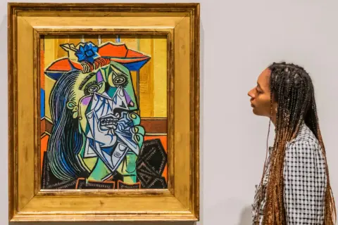 A woman gazes at a vibrant, cubist portrait, a striking example of obras de Pablo Picasso. The painting features a fragmented face with bold colors and sharp lines.