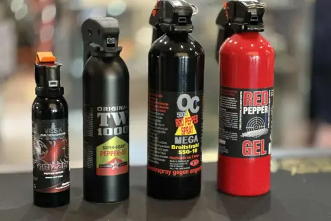 Cztery różne pojemniki z gazem pieprzowym, w tym jeden czerwony z napisem "RED PEPPER GEL".
