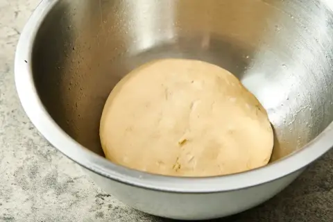 Gładkie, jasne ciasto na pizzę w metalowej misce, gotowe do wyrastania.