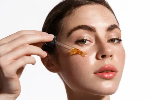 Una mujer aplica un sérum con ácido salicílico y vitamina C en su rostro.