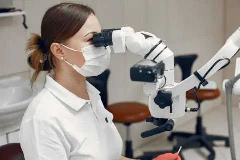 Dentystka w masce i rękawiczkach wykonuje leczenie kanałowe zęba krok po kroku, używając mikroskopu.