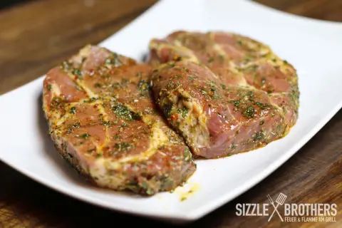 Zwei saftige Steaks, mariniert mit Kräutern und Gewürzen, liegen auf einem weißen Teller. Die Frage: Steak marinieren oder nicht?