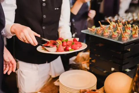 Kelner serwuje truskawki, prezentując różne metody serwowania potraw. Obok widać eleganckie przekąski.