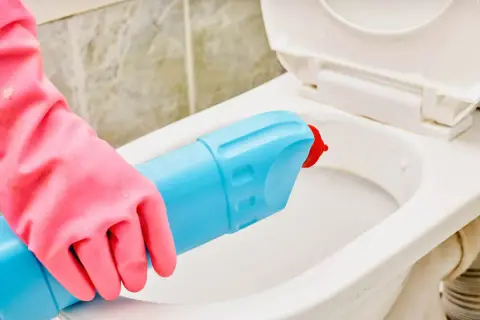 Mano con guanto rosa usa detergente per pulire il water incrostato.
