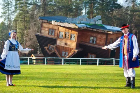 Para, gdzie jest dom do góry nogami? Para w strojach ludowych zaprasza do obejrzenia niezwykłego domu stojącego na dachu.