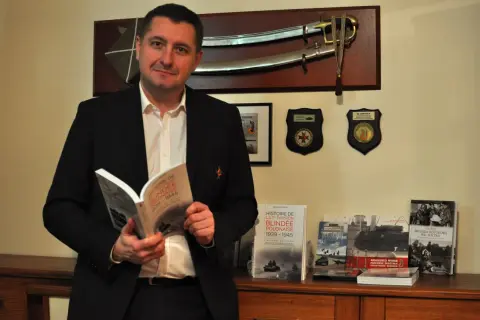 Un homme lit un livre sur l'histoire de la 1re division blindée polonaise. Le nom "Switek" pourrait être lié à l'origine de ce nom, peut-être un ancêtre ou un lieu.