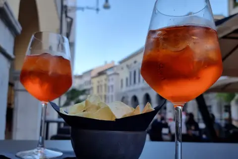 Dwa drinki Aperol Spritz i miseczka chipsów na stoliku. Czy alkohol podnosi cholesterol? To pytanie zadaje sobie wielu, popijając orzeźwiający drink.