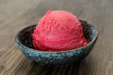 Ein Löffel Kirsch Eis in einer Schale auf Holztisch.