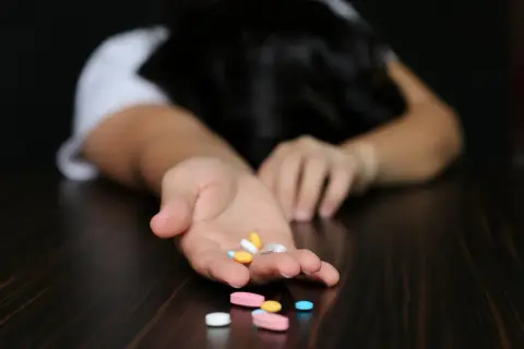 Dłoń z garścią tabletek, w tym alprazolam, na ciemnym blacie.