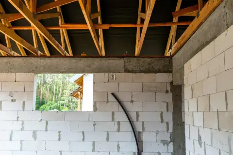 Widok wnętrza budowy z bloczków betonowych, widoczna konstrukcja dachu. To etap prac, który przybliża do momentu, jak zrobić wieniec budowlany.