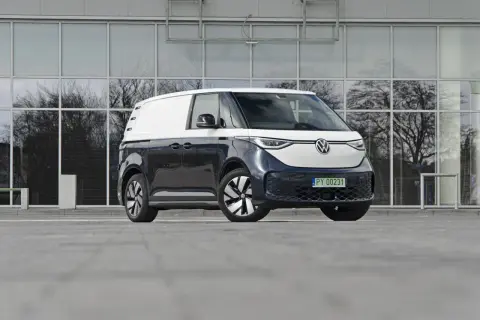 Dwukolorowy Volkswagen ID. Buzz 7 osobowy, zaparkowany przed nowoczesnym budynkiem z lustrzanymi oknami.