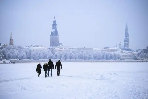Familie spaziert über zugefrorene Daugava in Riga, Lettland im Winter. Die Stadt mit ihren Türmen ist im Schnee versunken.